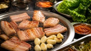 Korejský bůček grilovaný na stole s česnekem a omáčkou ssamjang (Samgyeopsal)