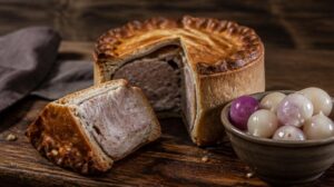 Tradiční vepřový koláč Pork Pie podávaný zastudena s nakládanou cibulkou